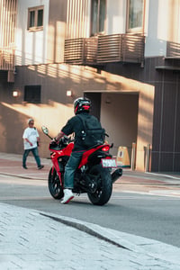 Back view of a biker riding a powerful red sport motorcycle on a city street
