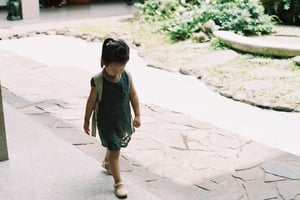 Bé gái đeo balo chập chững bước đi trên lối vào sân vườn ngập nắng