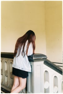 Back view of a young woman with long hair in denim jacket leaning on a vintage staircase railing