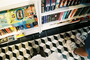 Top down POV of a person standing on 3d patterned floor tiles next to bookshelves