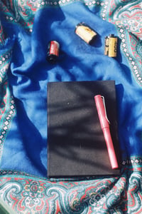 Black notebook, fountain pen, and vintage 35mm film rolls on a blue patterned scarf