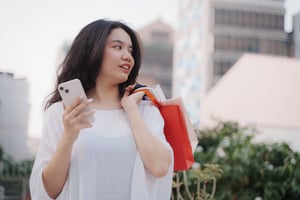 Woman using smartphone while holding over the shoulder some shopping bags