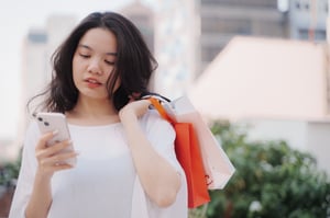 Woman using smartphone while holding over the shoulder some shopping bags