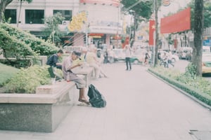 Cụ ông ngồi thư giãn đọc báo bên vỉa hè trung tâm Sài Gòn