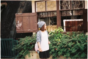 Young woman in beanie hat standing by a vintage wooden window of an old house.