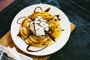Delicious sweet waffle topped with peach slices, whipped cream and chocolate syrup