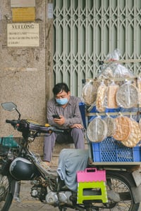 Người đàn ông bán bánh tráng đang nghỉ ngơi lướt điện thoại