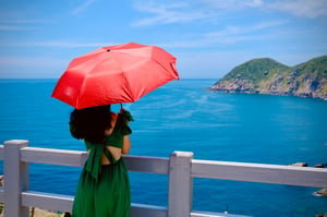 Girl with red umbrella looking out to sea